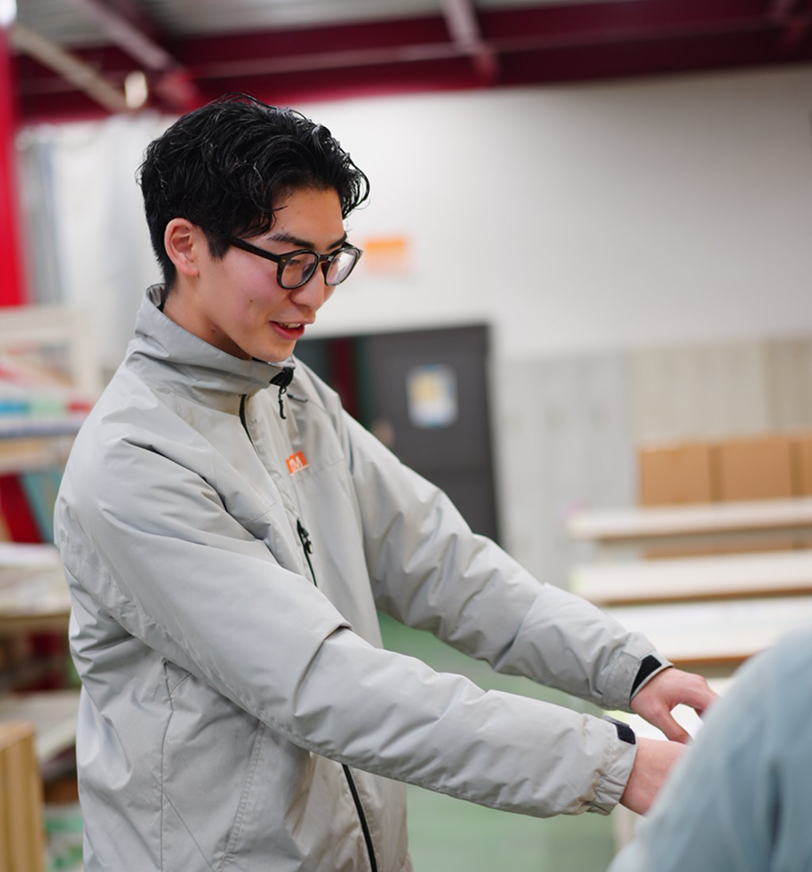 工場内で作業着姿の若い男性が笑顔で同僚とやり取りしている場面