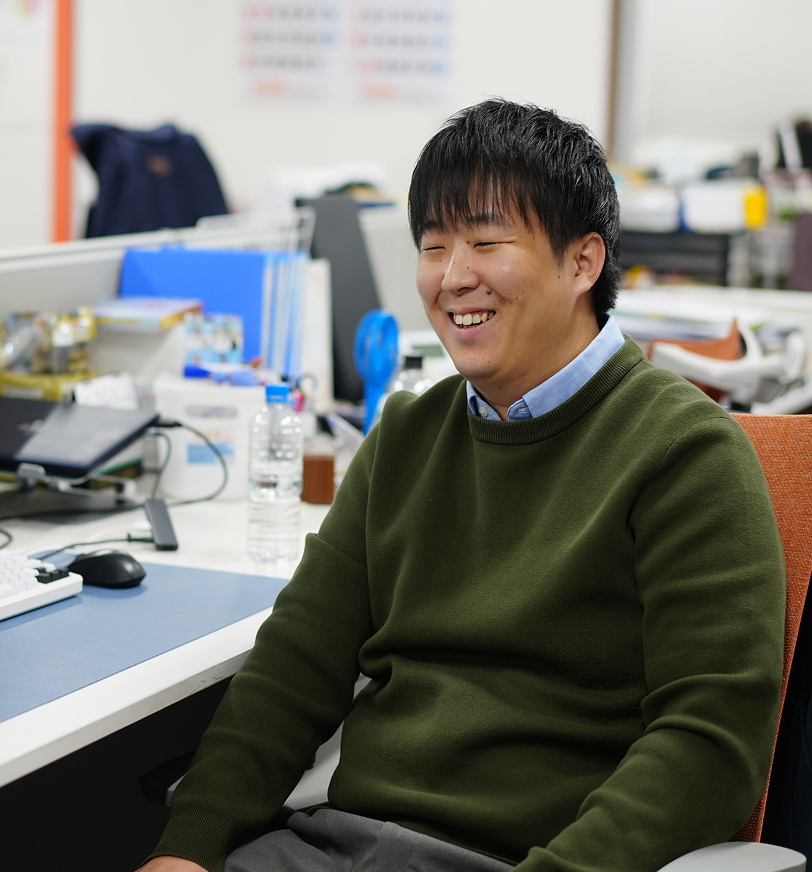 パソコンや資料に囲まれながら笑顔を見せているオフィス風景